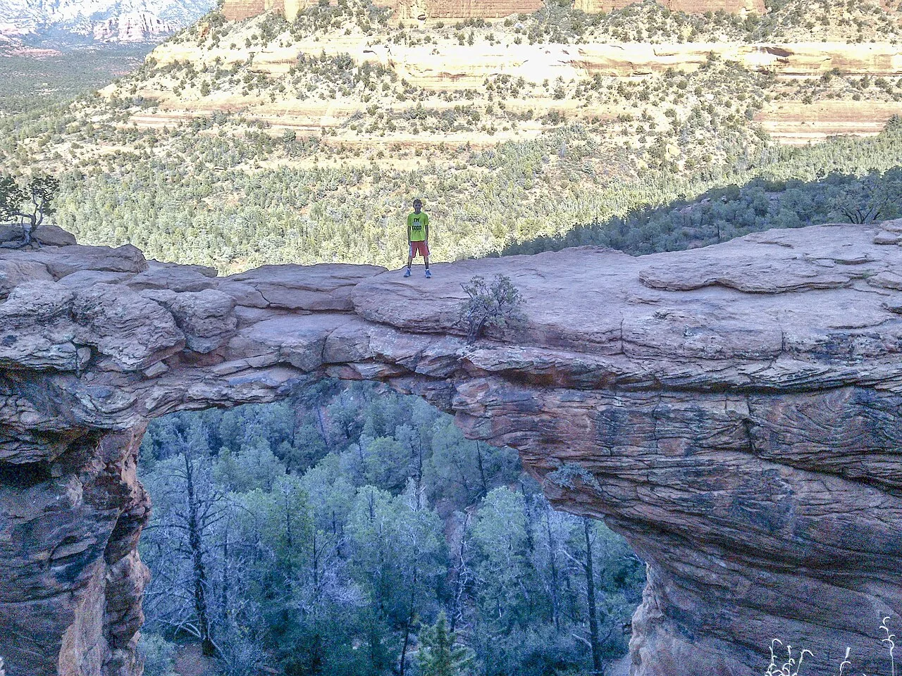Hiker standing on the natural sandstone arch of Devil's Bridge near Sedona